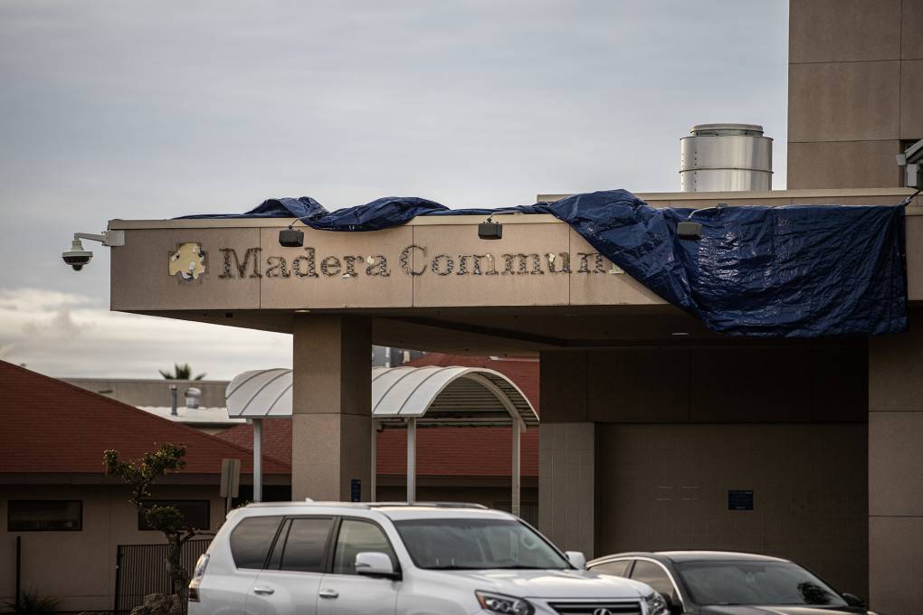 A sign of a partially covered building with a tarp reads "Madera Community."