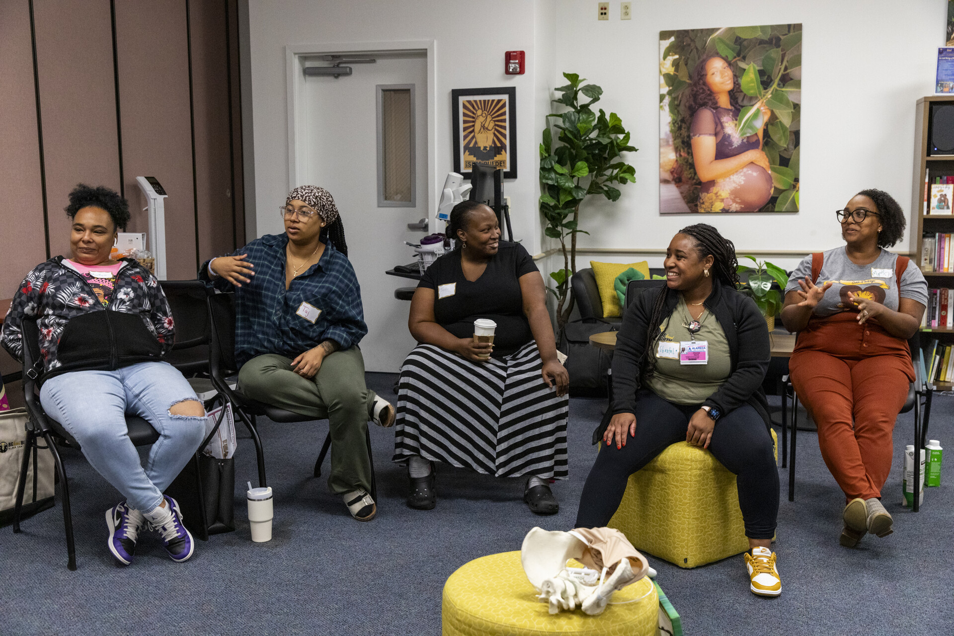Five African American women sit in a room, smiling and conversing.