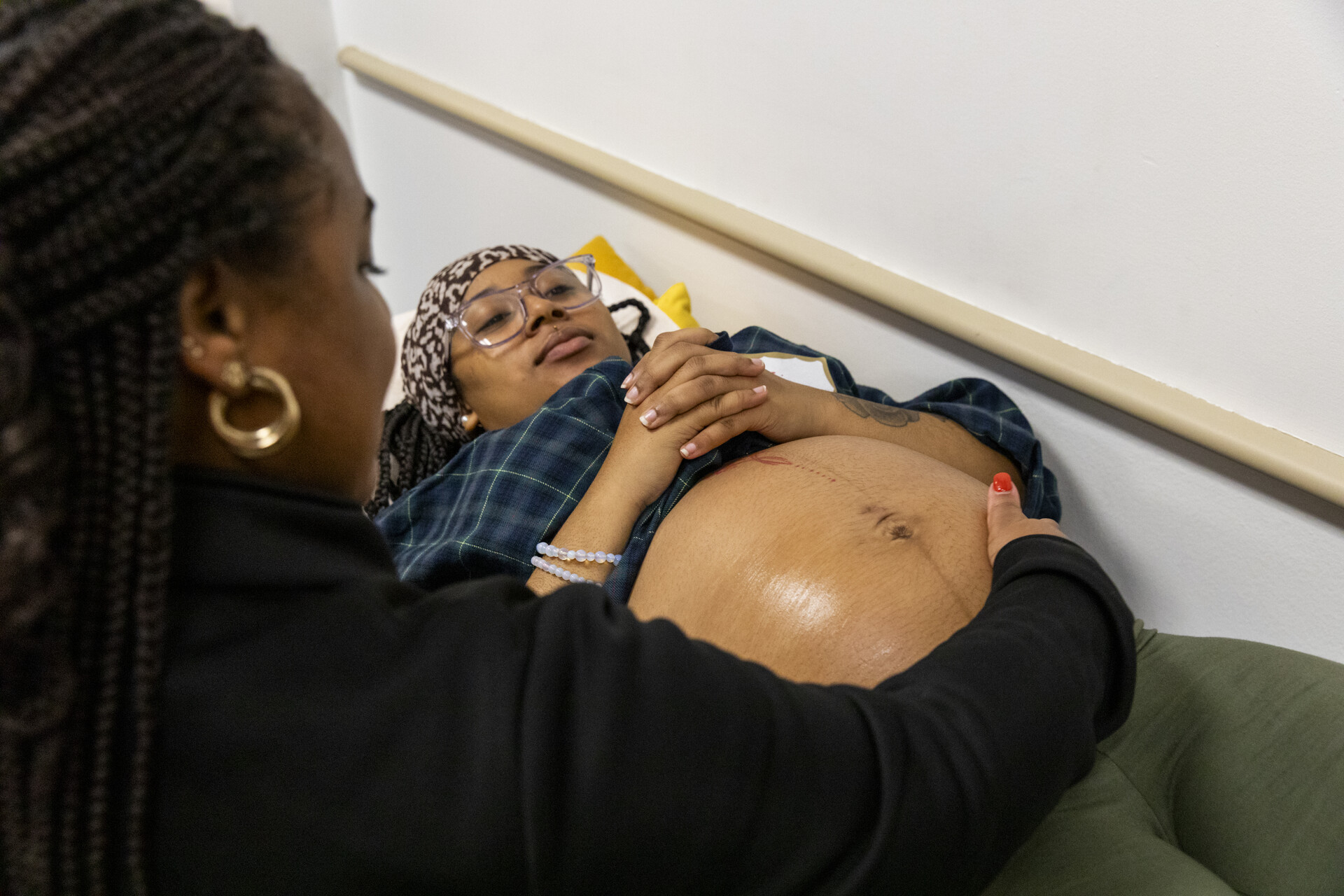 A pregnant woman is laying down and receiving prenatal care from another woman.