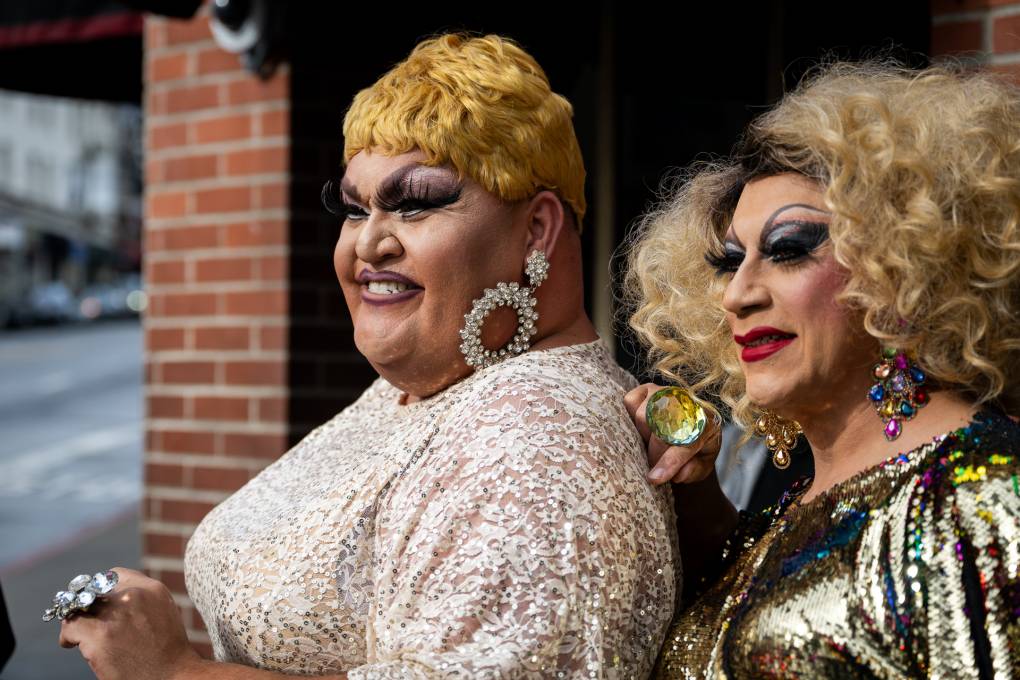 Two drag artists smile as they stand on the street.