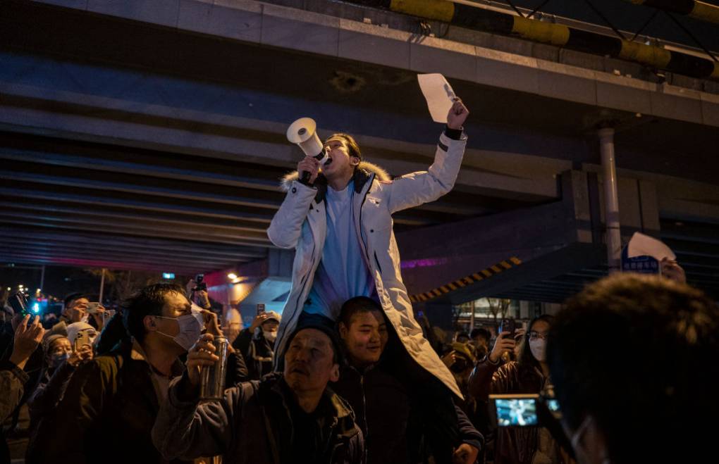 A protester sitting on someone's shoulders, yells into a bullhorn.