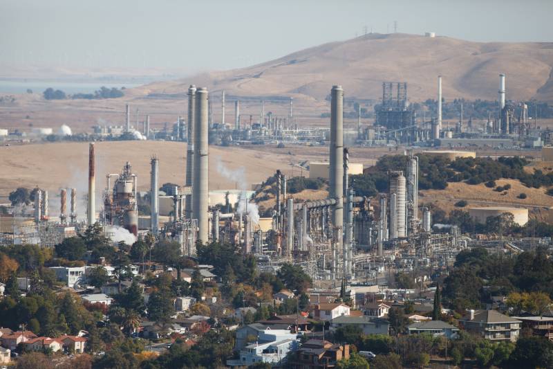 A view of two large industrial facilities — both refineries — each with many smokestacks - with hills in the background.