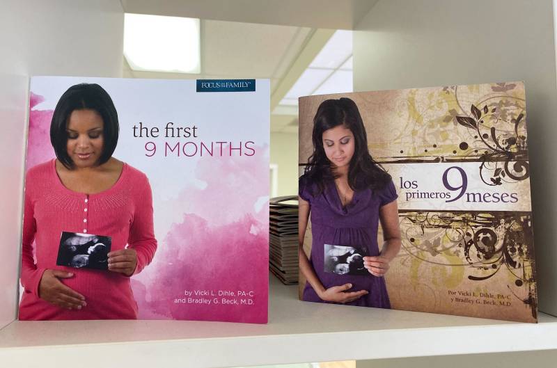 pamphlets in English and Spanish on a shelf show a Black woman and a Latina woman who are pregnant. The pamphlet is titled 