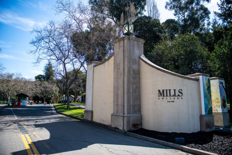 The main entrance to the leafy Mills College campus, a rounded concrete wall with "Mills" written on it.
