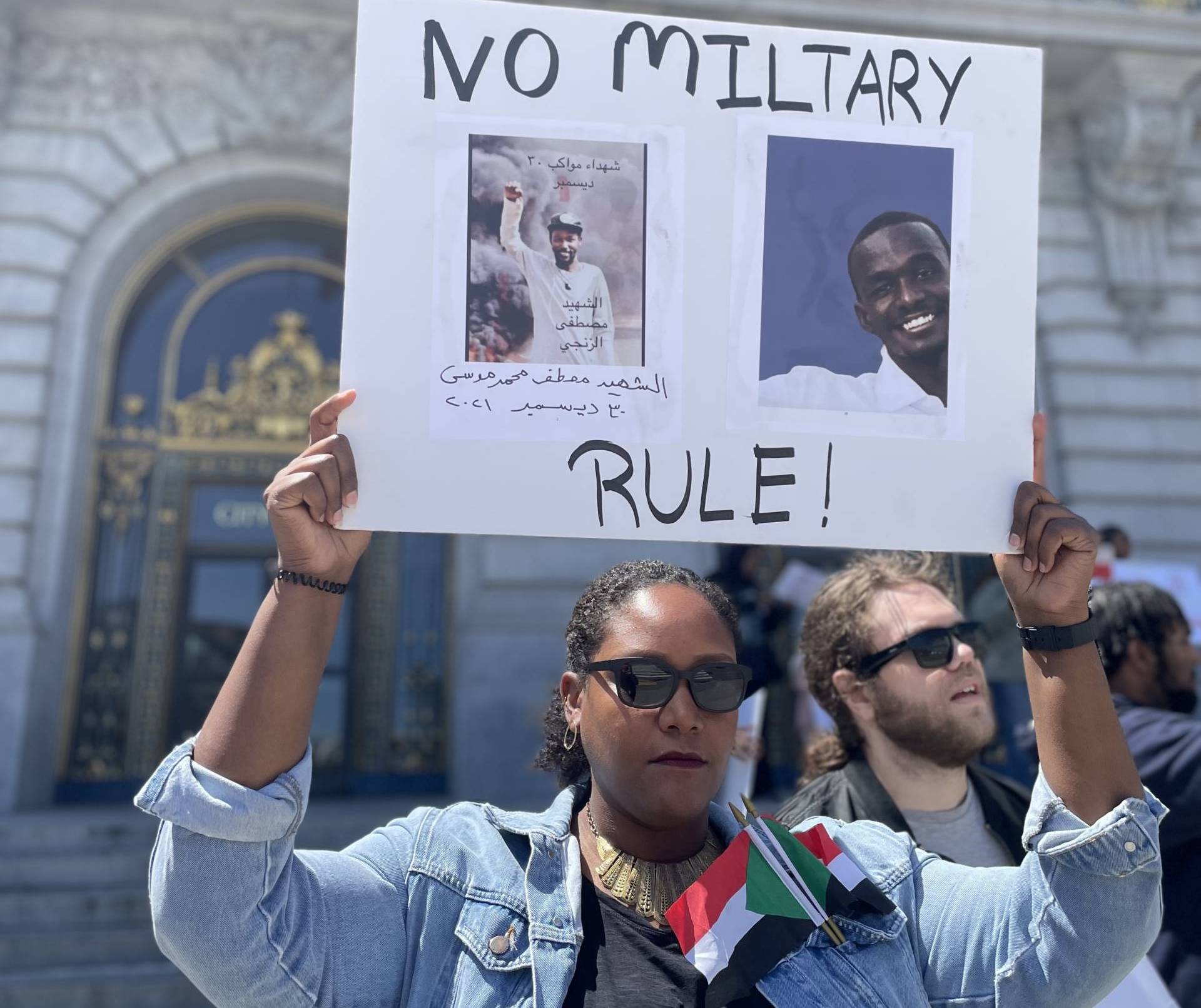 A Sudanese American woman holds a sign that reads "No Military Rule" outside SF City Hall.