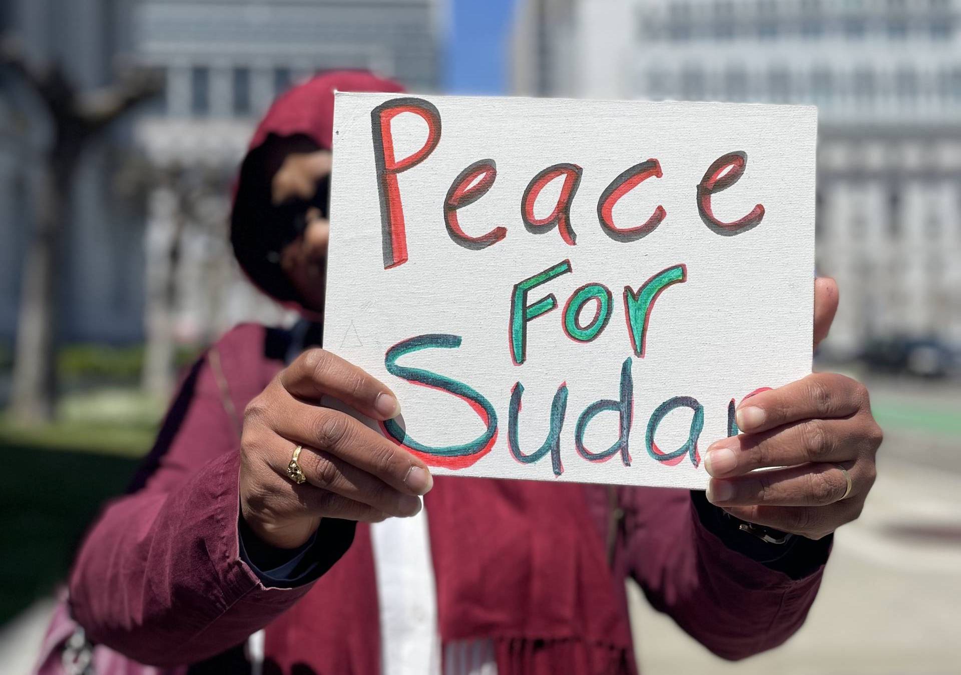 A Sudanese American woman holds a sign that reads "Peace For Sudan"