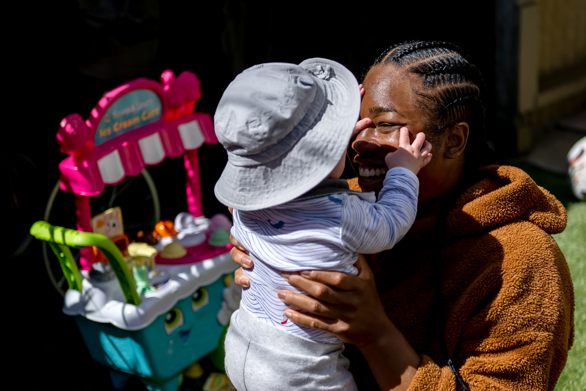 A Black woman holds a small child up to her face while smiling. The child touches her face.