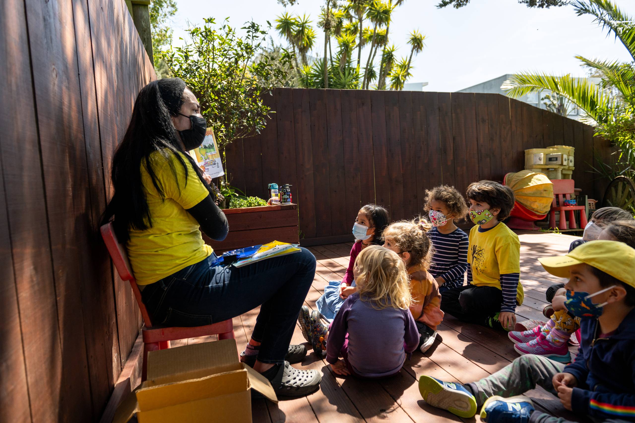 A teacher reads to children gathered around her.