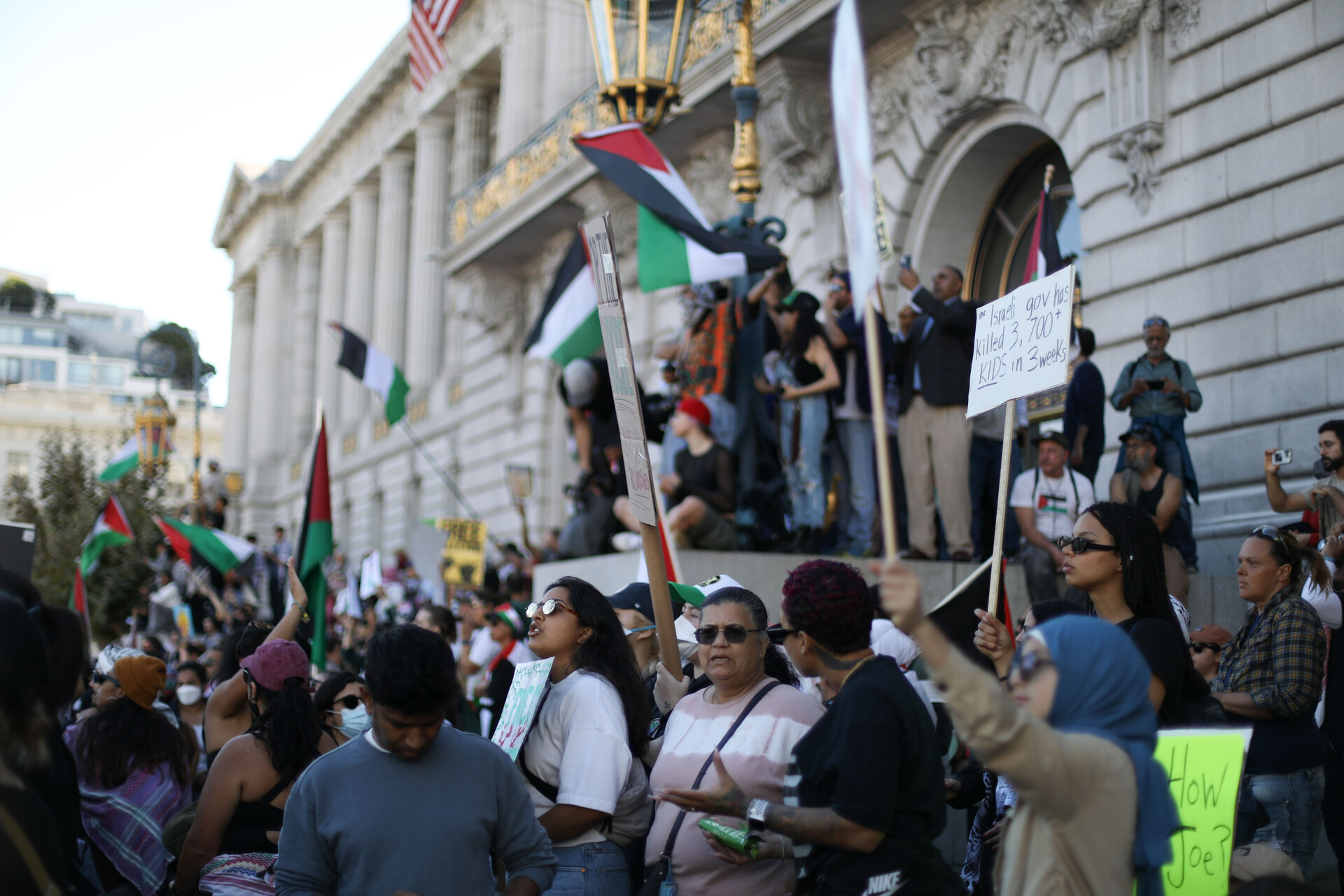 A crowd of protesters with signs and Palestinian flags gathered on the steps of San Francisco City Hall.