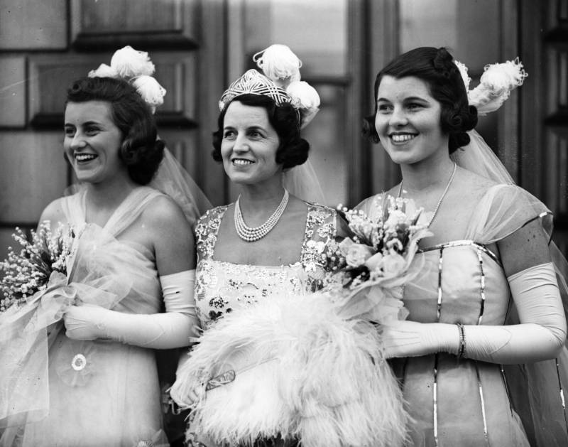 A black and white image of a mother and her two daughters, all dressed in elegant 1930s evening wear, all smiling.