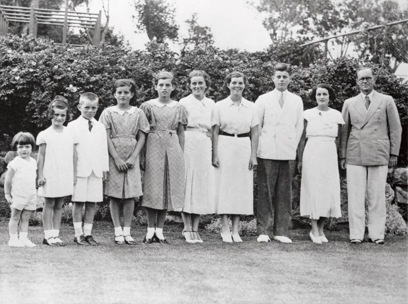 A couple stands in a garden with, to their left, their eight children standing in descending order of height.