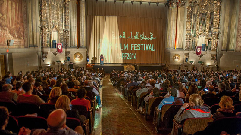 a shot of the interior of a movie theater, the screen shows that this is the 2014 Arab Film Festival at San Francisco's Castro Theatre