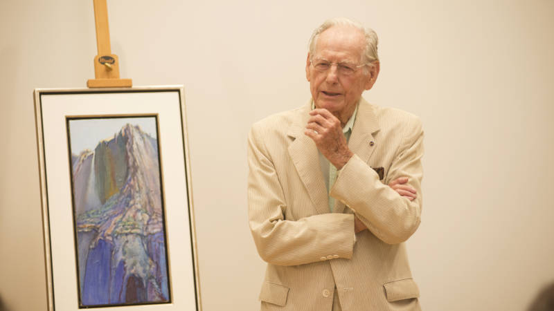 Wayne Thiebaud in a white suit, standing near a painting
