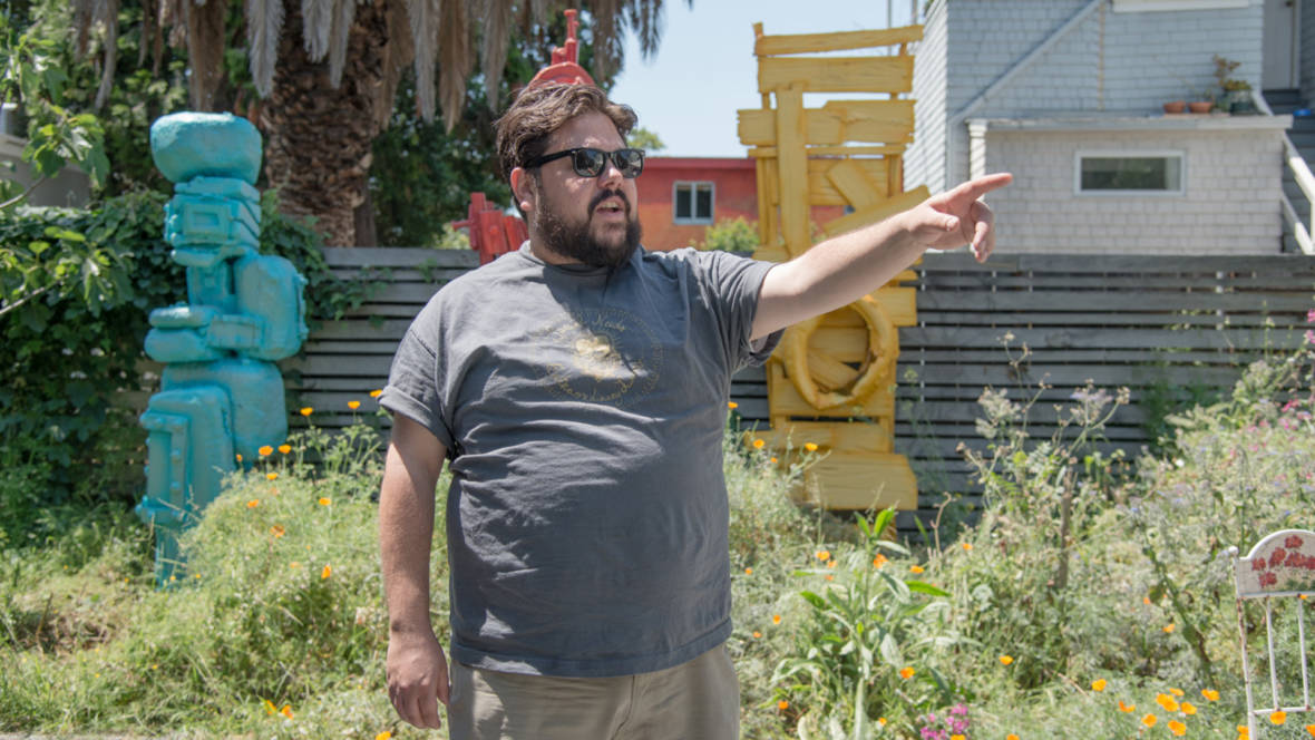 Joey Enos stands in the yard outside his Oakland home and studio, three sculptures in the background.  Photo: Graham Holoch/KQED