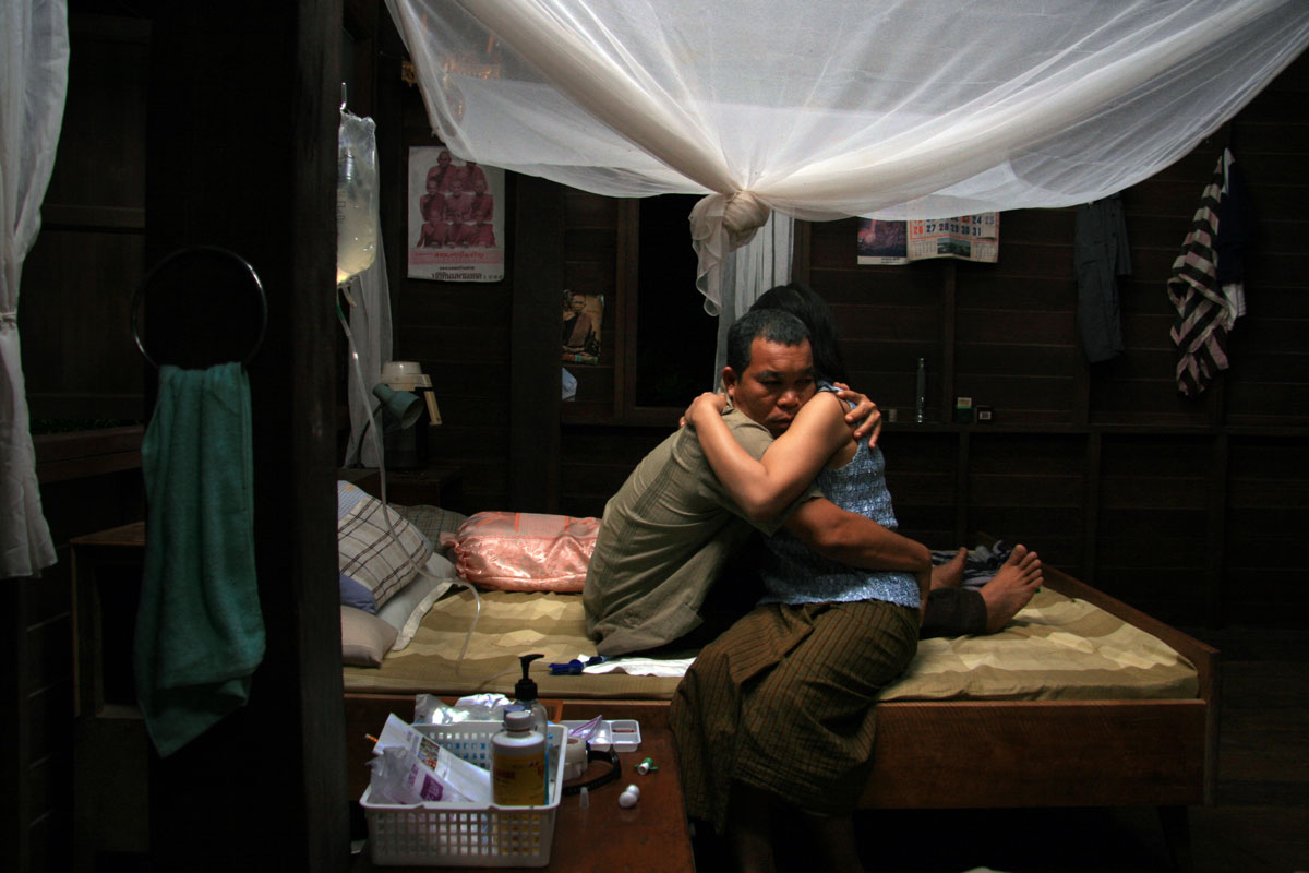A man connected to an IV hugs a woman on a bed.