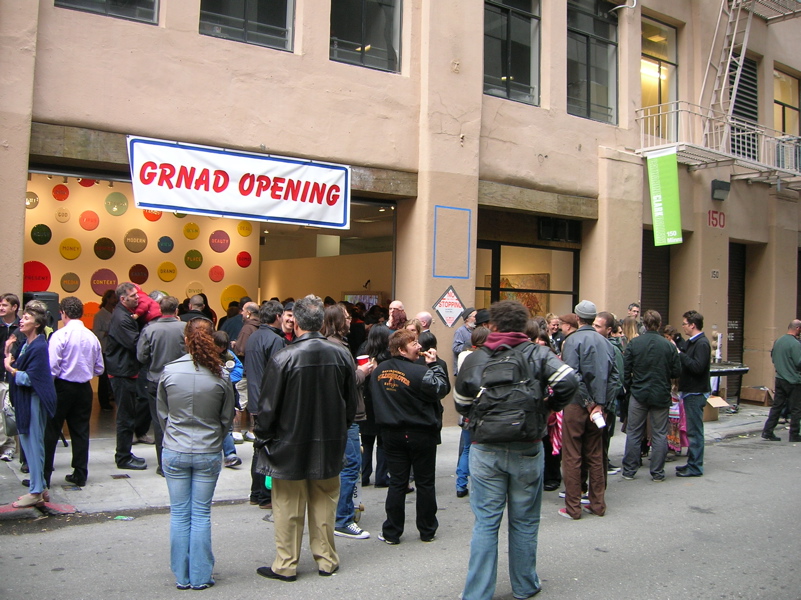 People gathered outside the gallery on MInna Street, a banner reads "GRNAD OPENING" over the roll-up door.
