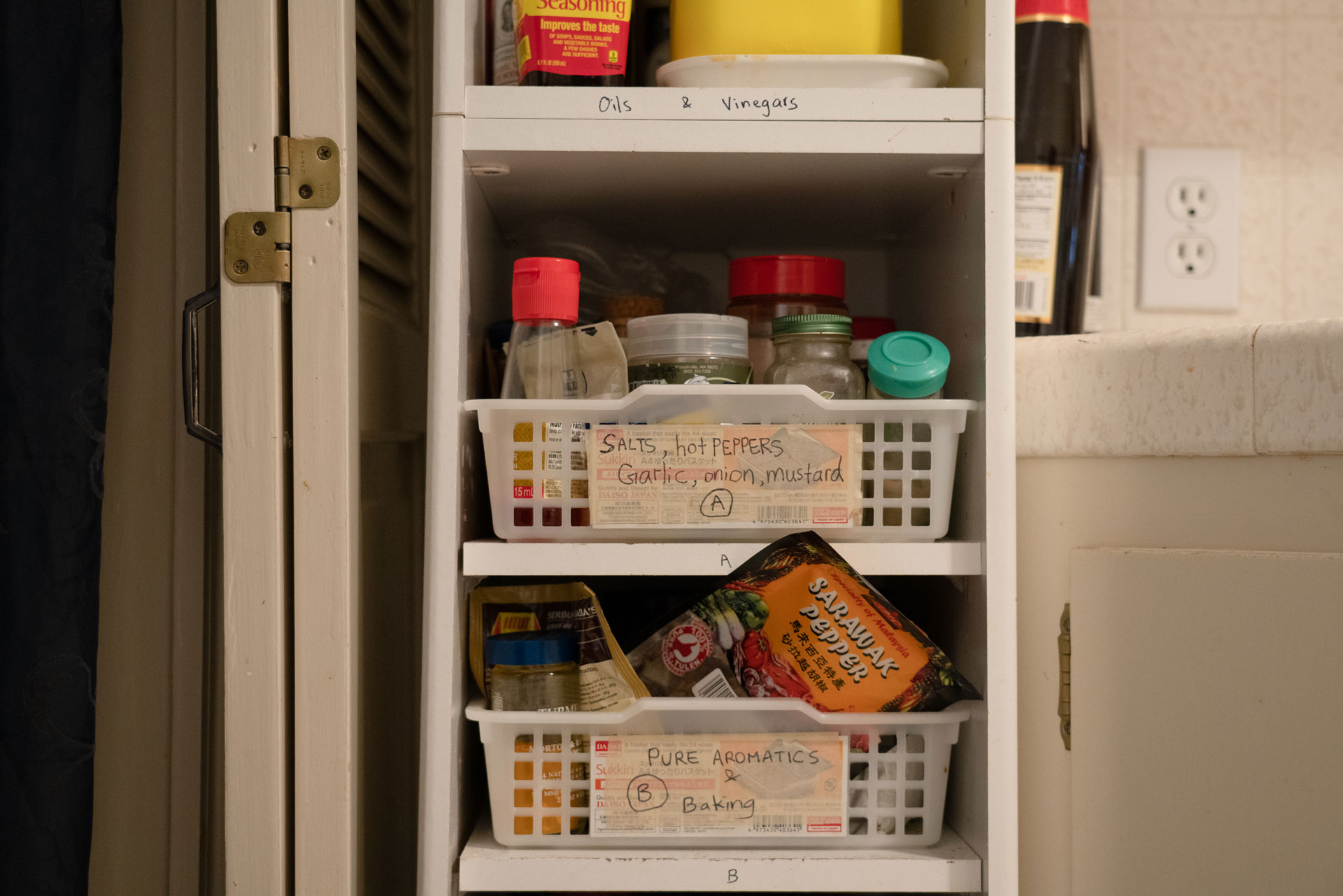 Labeled baskets of spices sit in a white shelf in the kitchen.