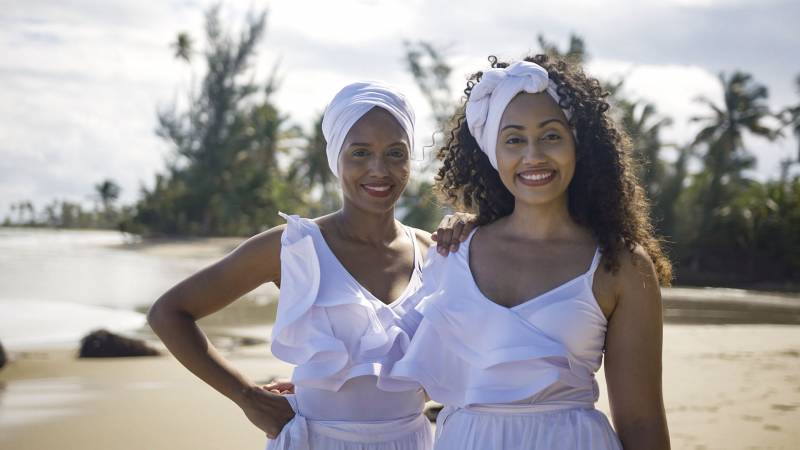Afro-Puerto Rican sisters Mar and María Cruz stand on a picturesque beach with palm trees near San Juan, Puerto Rico.