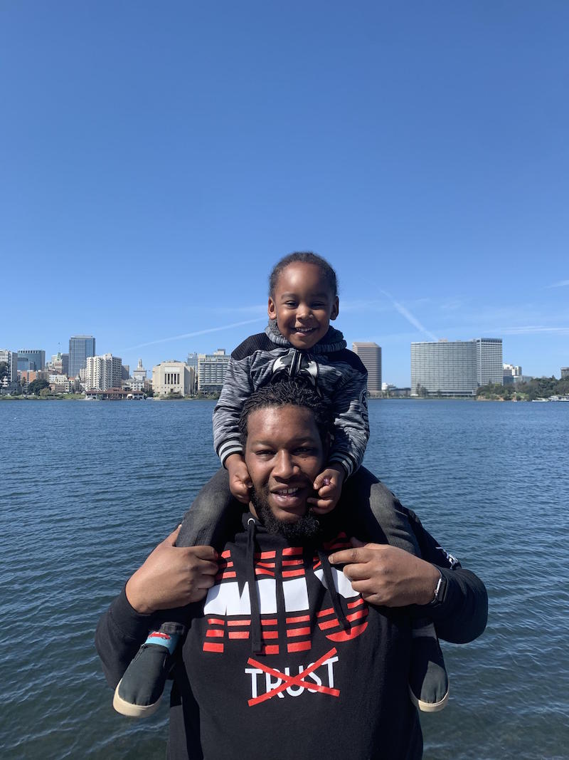 A father and son pose in front of Lake Merritt and the Oakland skyline.
