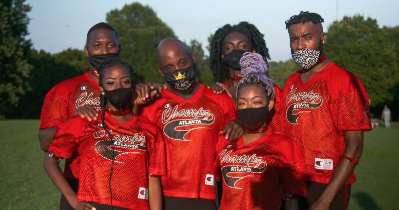 Members of Dance Champz of Atlanta pose in red customized jerseys that read "Champz Atlanta". They are wearing fabric masks that cover the lower half of their faces. This photo is taken at sunset in Piedmont Park in Atlanta, GA.