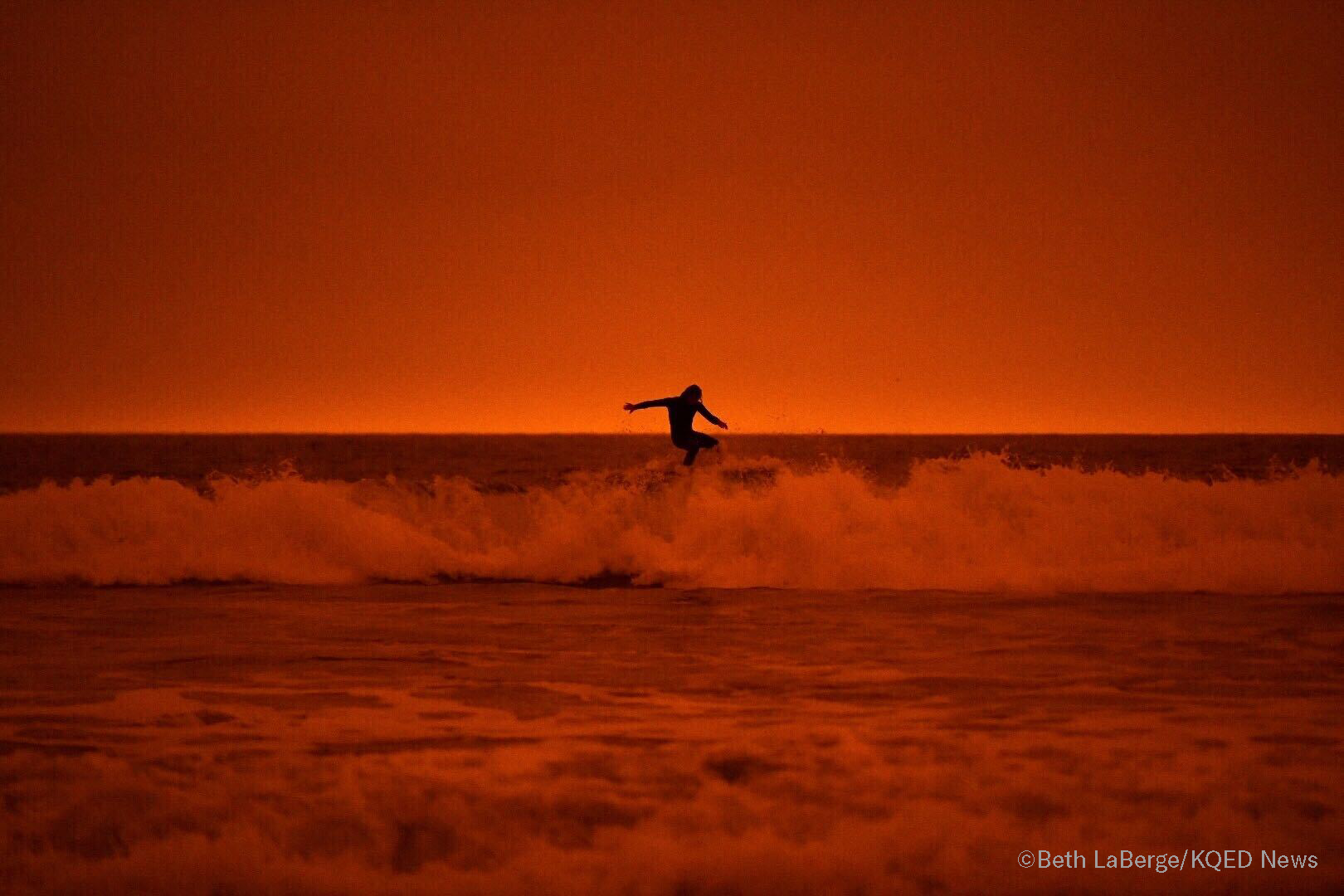 A surfer rides the waves of Ocean Beach in San Francisco under smoke-filled orange skies, on Sept. 9, 2020.