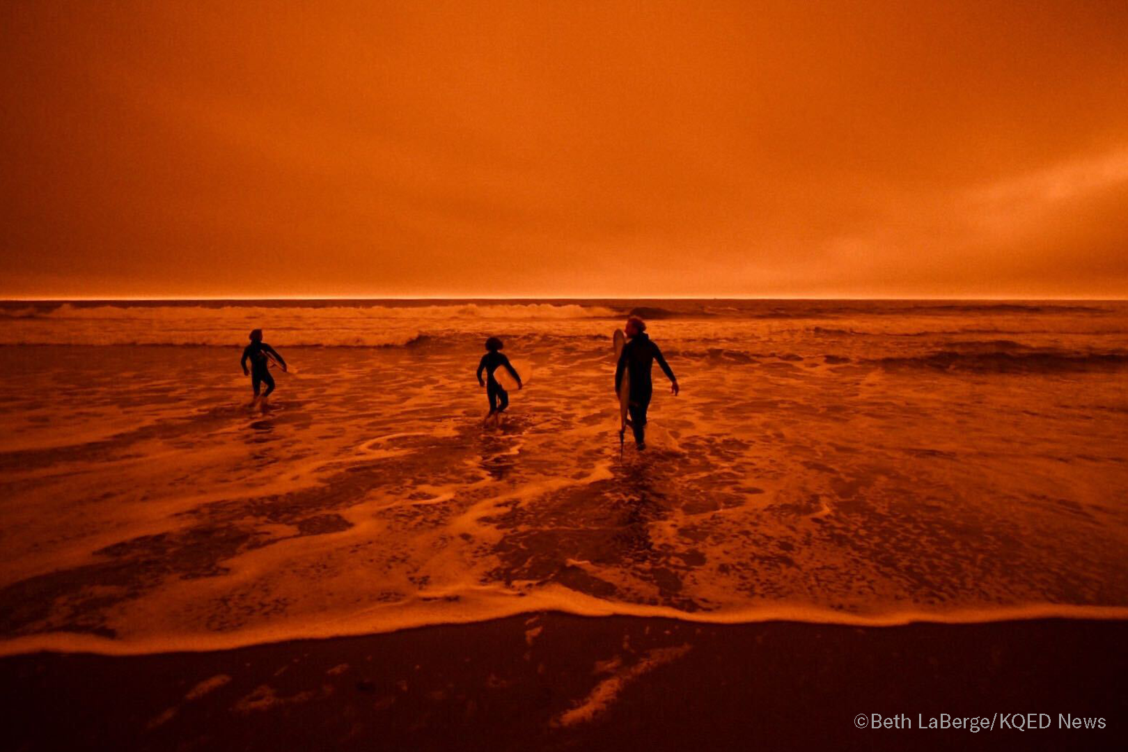 Surfers head for the the waves of Ocean Beach in San Francisco under smoke-filled orange skies, on Sept. 9, 2020.
