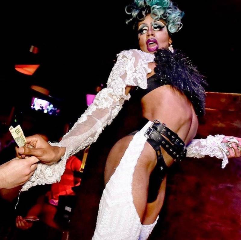 A drag performer wearing lace, faux fur and a garter belt collects a tip from a fan.