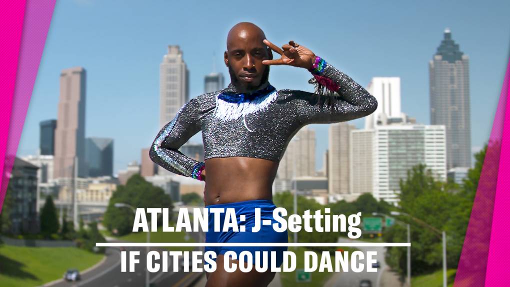 Black male dancer poses in sparkly grey top and bright blue shorts with the Atlanta, GA skyscrapers in the background.