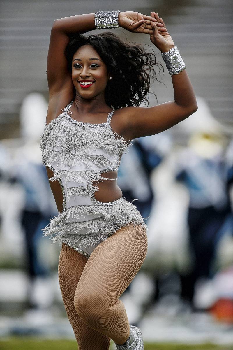A close-up of a Prancing J-Settes dancer posing in a silver bodysuit with a fringe, nude fishnet stcokings and silver sequin cuffs on her wrists.