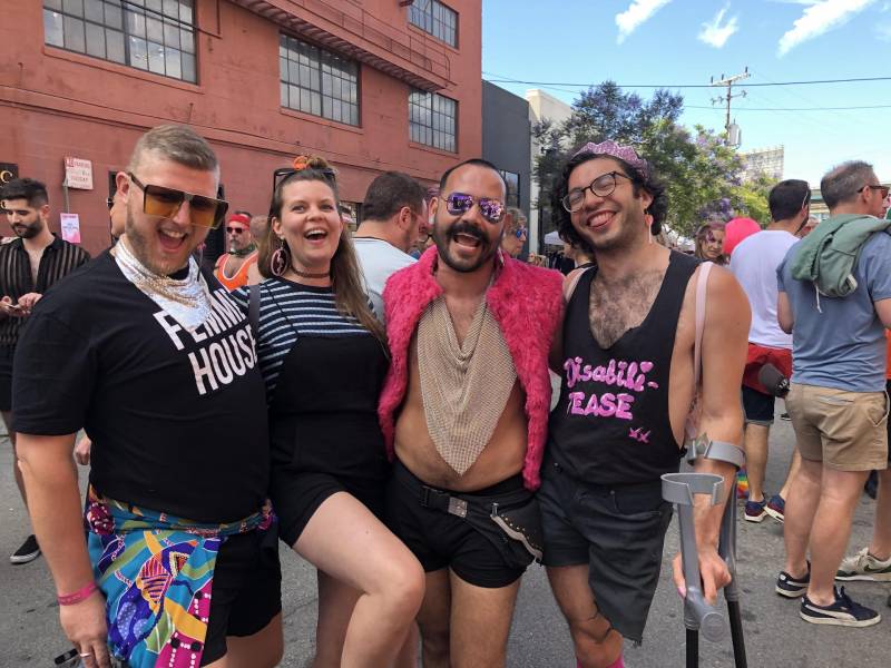 Four smiling friends pose at a Pride celebration.