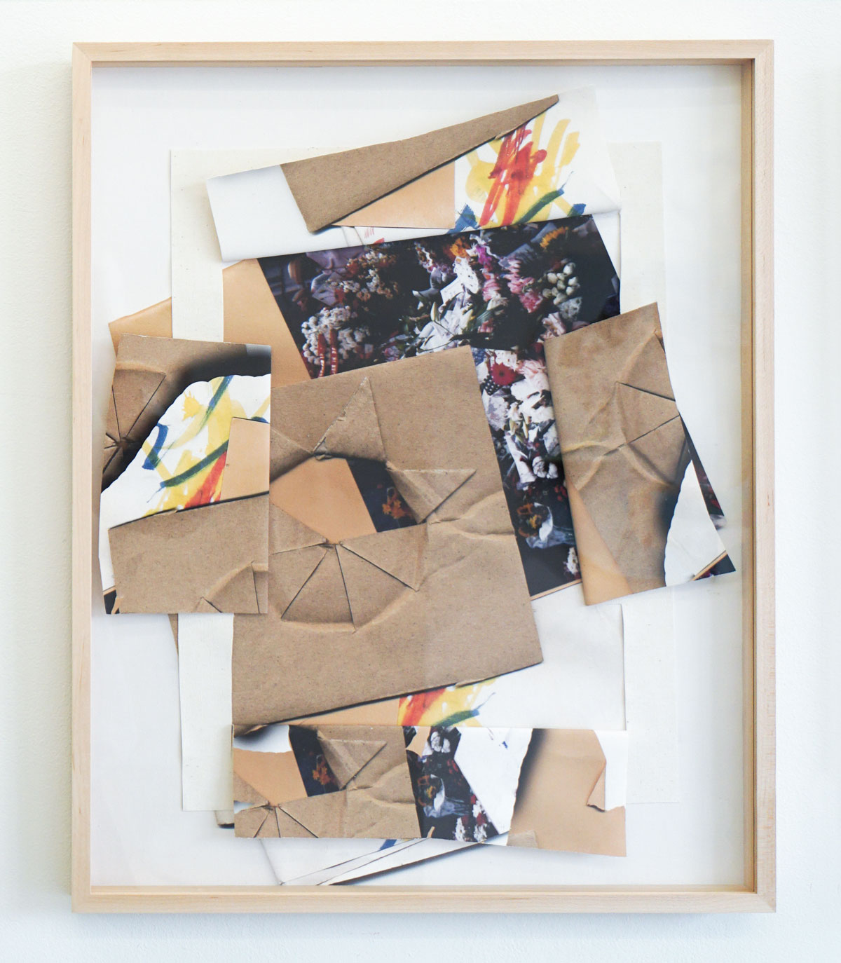 Light wood frame around a mixed media work, collaged images of brown paper cut and folded in a star pattern, childlike marker drawings and a photograph.