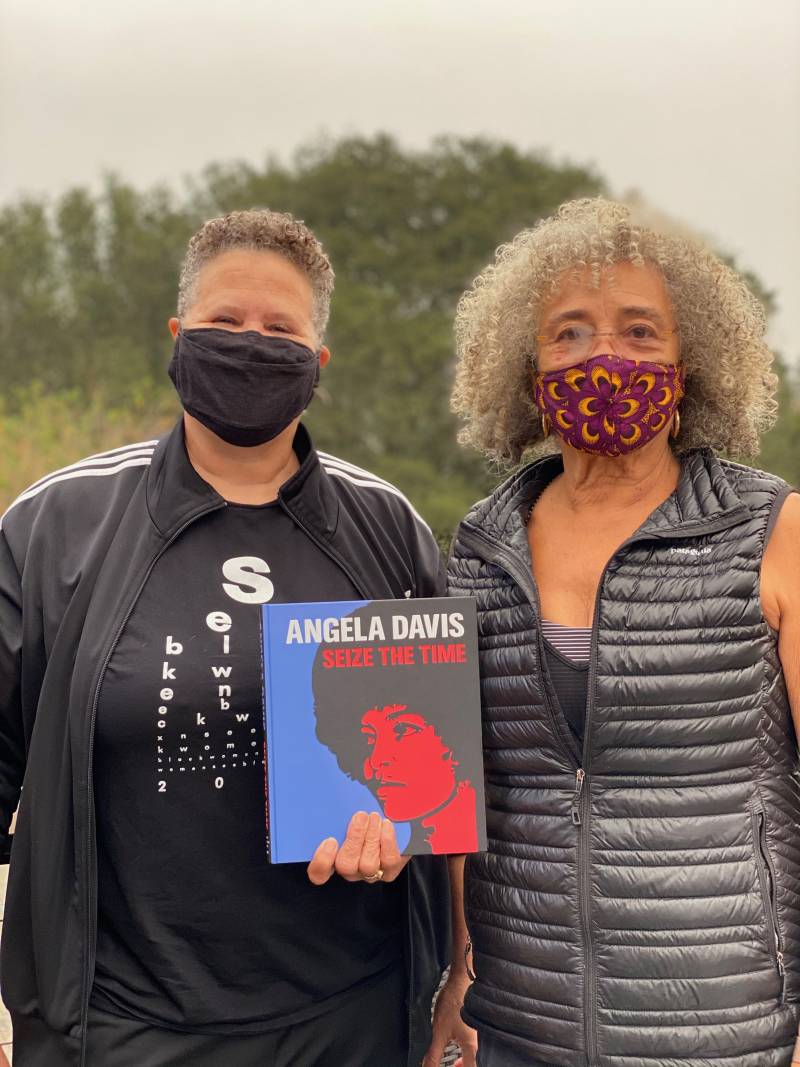 Lisbet Tellefsen and Angela Davis wear masks to protect from COVID-19 as they pose for a photo while holding a copy of the book, 'Seize the Time.'