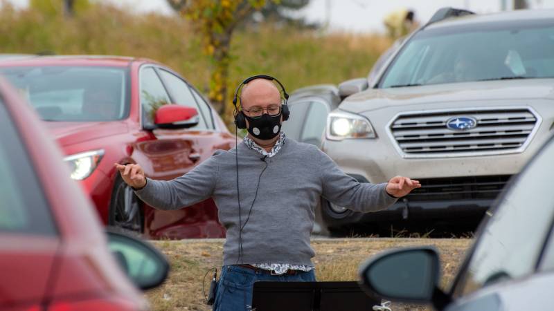 Shantz conducts Luminous Voices' first car concert, on Oct. 4, 2020. Audience vehicles are seen parked to behind him.