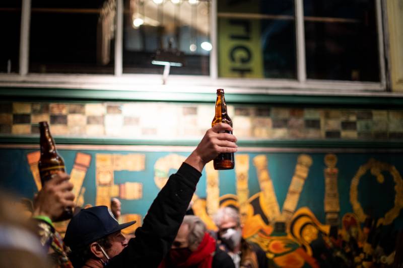 Bottles of beer are raised in the air during a cheers for Lawrence Ferlinghetti outside of City Lights Books on Feb. 23, 2021.