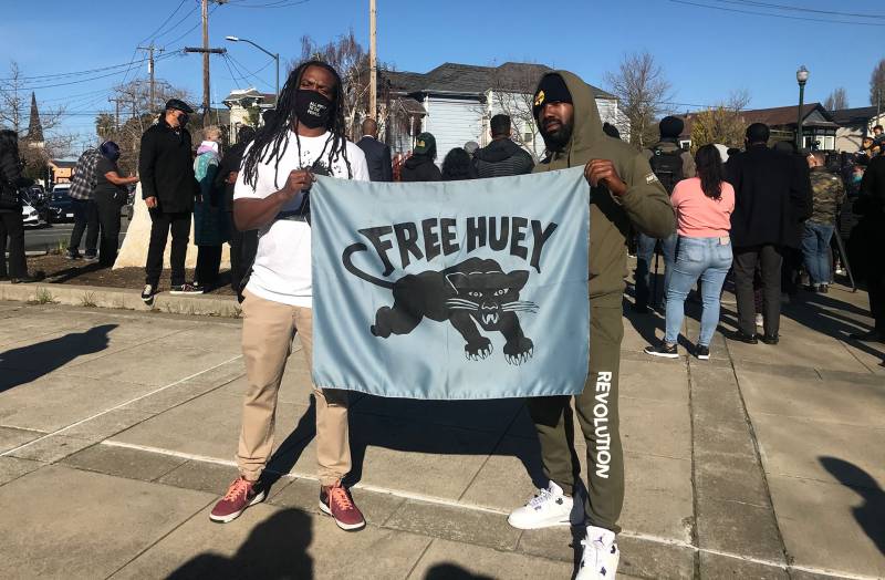 Two men hold a 'Free Huey' banner at the newly christened Huey P. Newton Way in West Oakland, Feb. 17, 2021. 