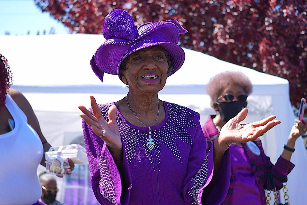 Marcella Hubbard smiles as she stands and cheers as people drive by in celebration of her 100th birthday.