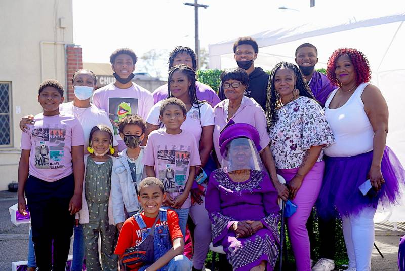 Mrs. Hubbard sits in the center as family members gather around her for a photograph. Almost everyone is wearing purple. 
