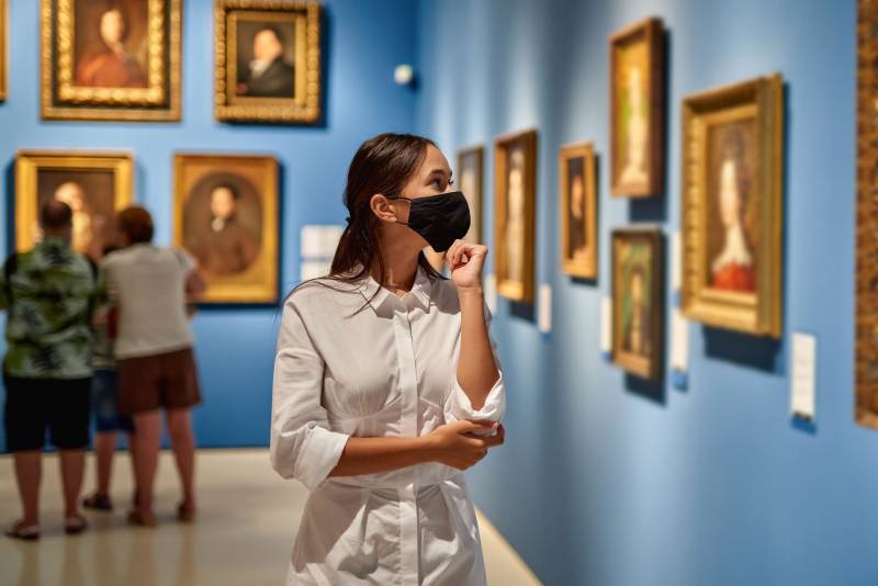 A woman in a mask looks at art in a museum