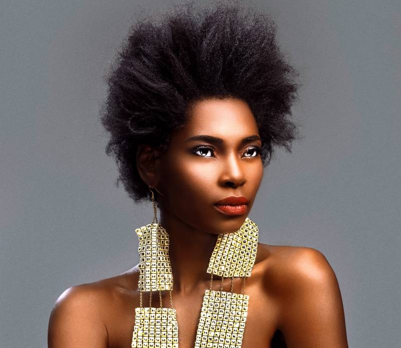 A woman with bare shoulders, Afro hair and large earrings gazes into the distance.