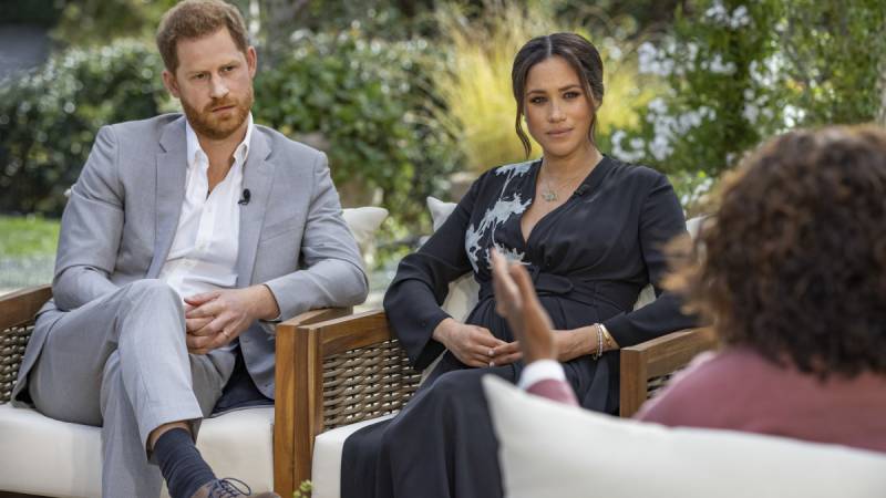 Prince Harry and Meghan Markle sit in a garden opposite their interviewer, Oprah.