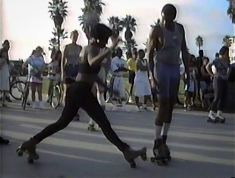 Female roller skater about to do a split at Venice Beach, CA. Still from a homemade video from 1990s.