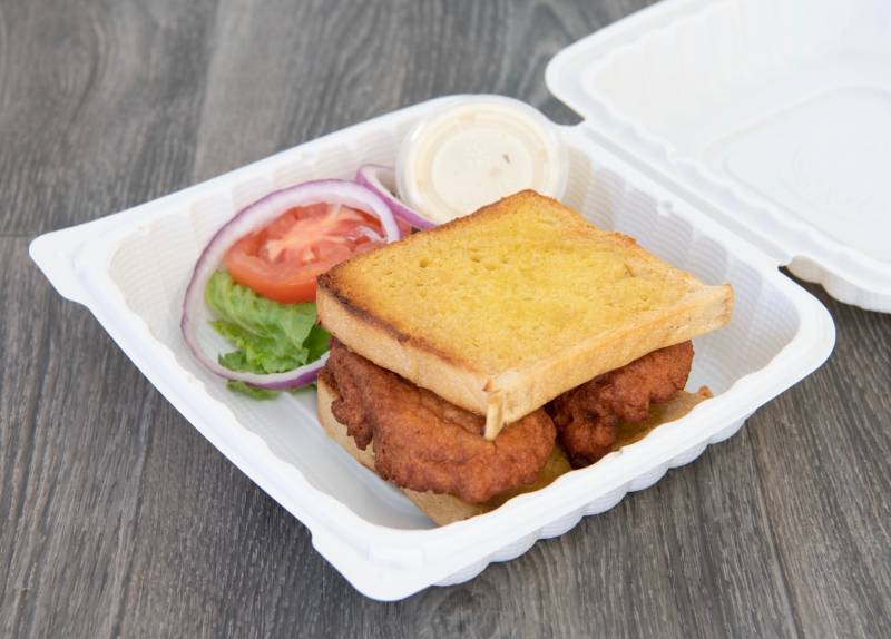 Takeout container with an akara burger: bean fritters between sliced Ghanaian bread.