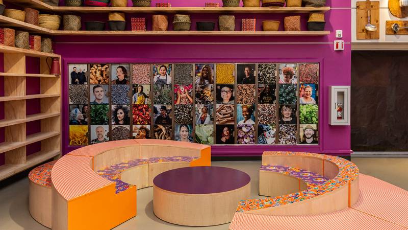 A community gathering area, colorfully decorated with curved banquette seating and a photo collage on the wall. 