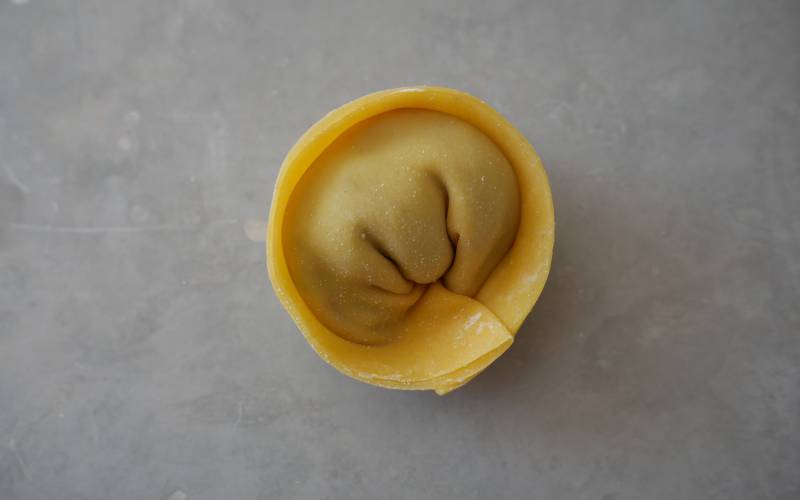 Close-up of an uncooked five-spice soup dumpling, which is shaped like a wonton.