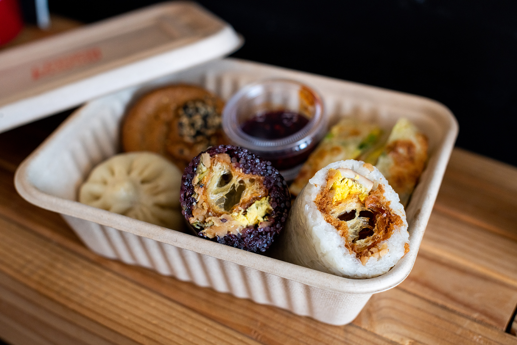 A takeout box with sticky rice rolls, scallion egg pancake, and other Taiwanese breakfast items from Taiwan Bento.