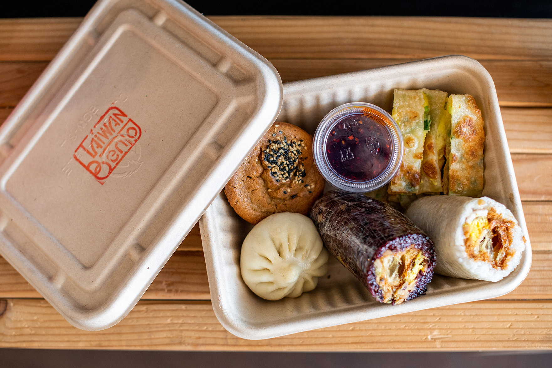 Overhead view of a takeout box with sticky rice rolls, scallion egg pancake, and other Taiwanese breakfast items from Taiwan Bento.
