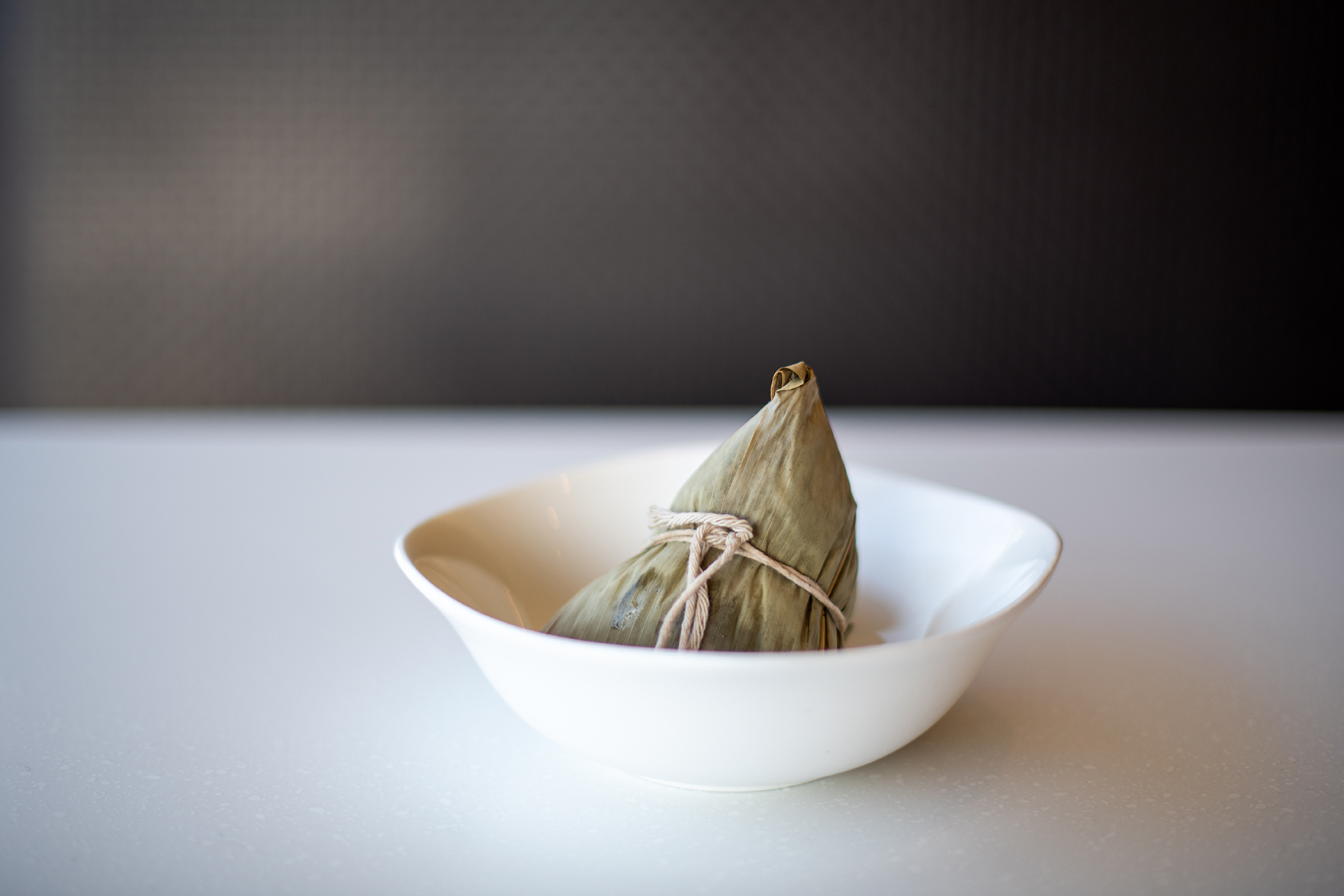Taiwanese bah tsang (or leaf-wrapped rice dumpling) in a white bowl on a white countertop.