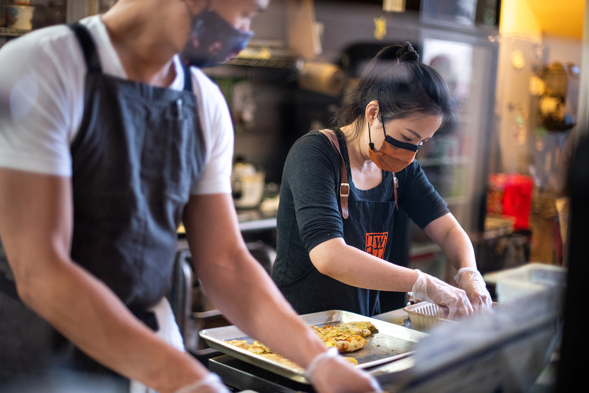 Stacy Tang (right), wearing a face mask, prepares scallion egg pancakes, or dan bing, during one of her restaurant's breakfast pop-ups.
