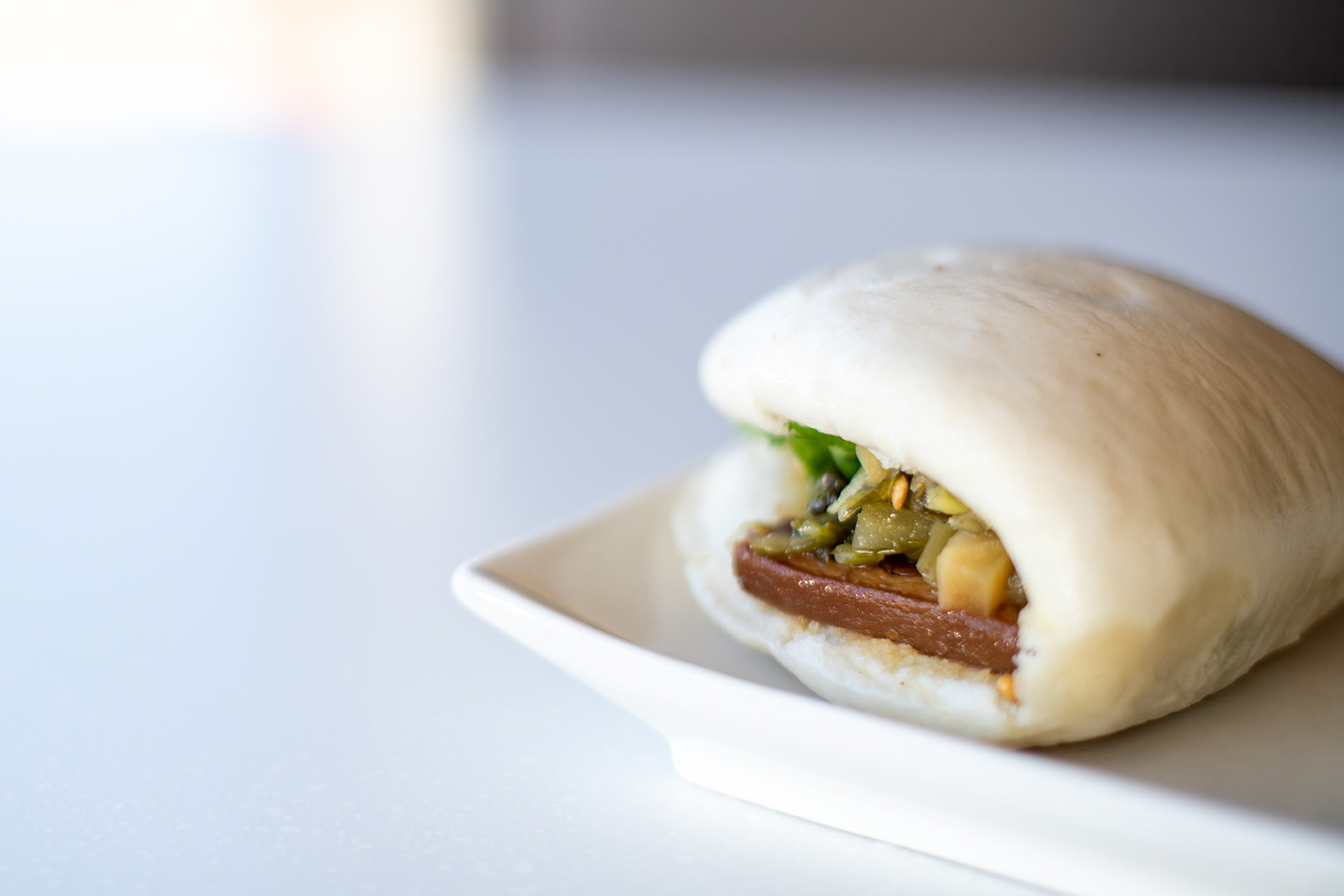 A traditional pork belly gua bao on a plate, on a white countertop.