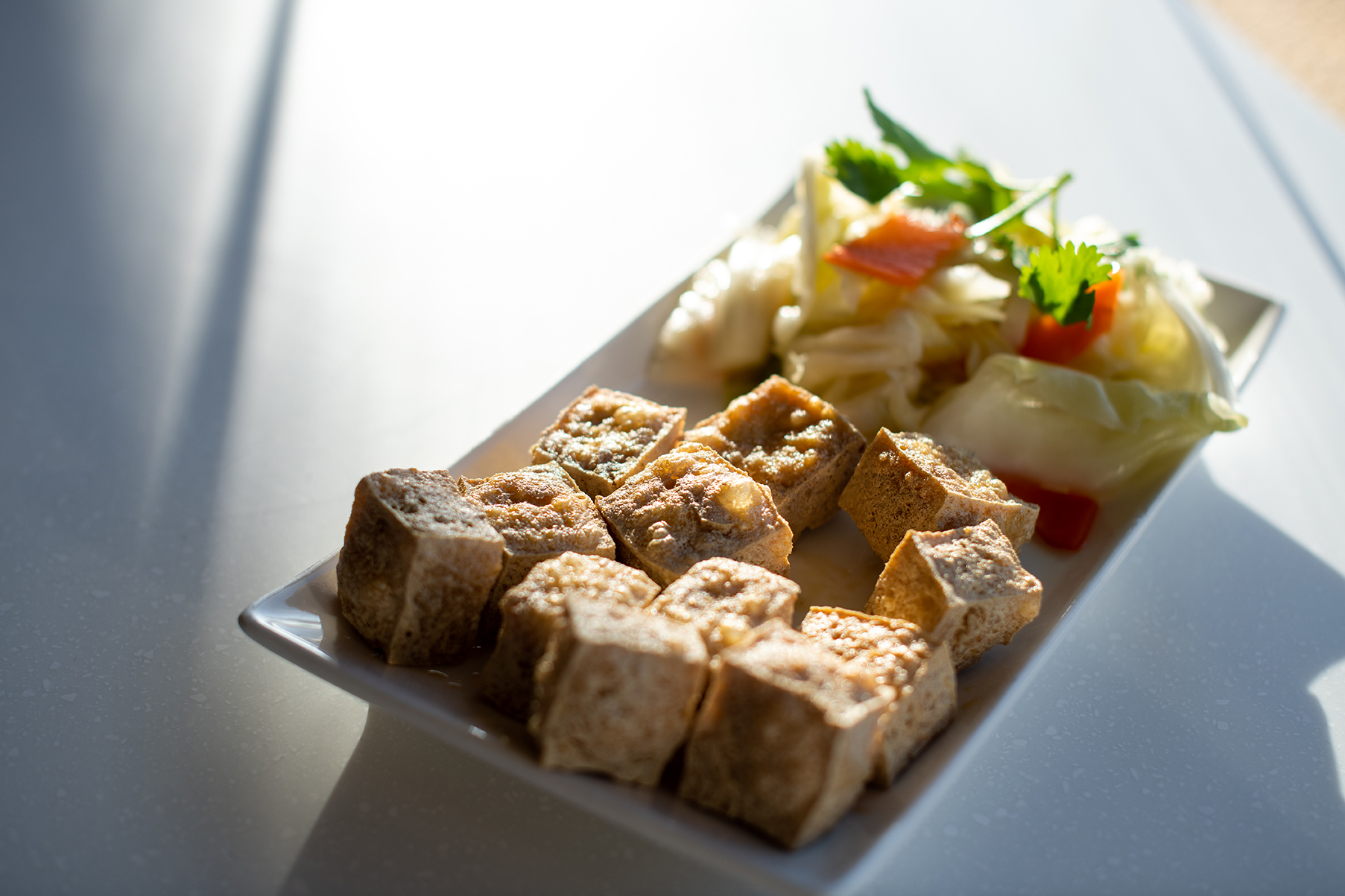 A plate of fried stinky tofu with a side of pickled cabbage on a white countertop.